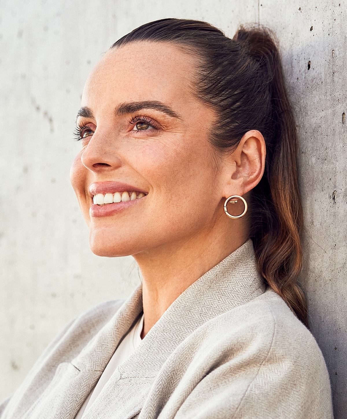 Smiling woman with hoop earrings against wall.