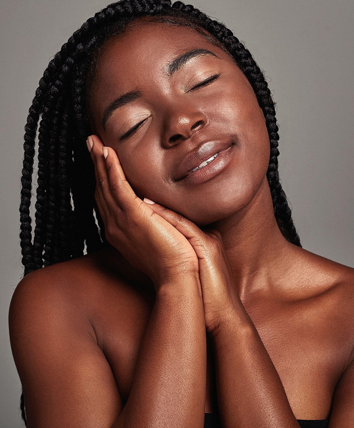 Smiling woman with braided hair, eyes closed.